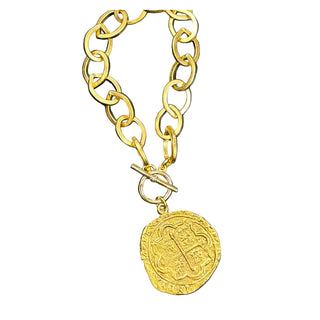 Gold chain bracelet with a vintage-style coin pendant on a dark background