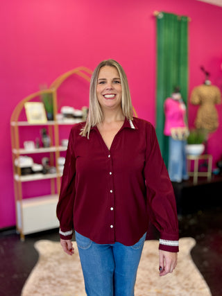 Woman wearing a burgundy blouse and blue jeans standing in a room with pink walls and shelves.